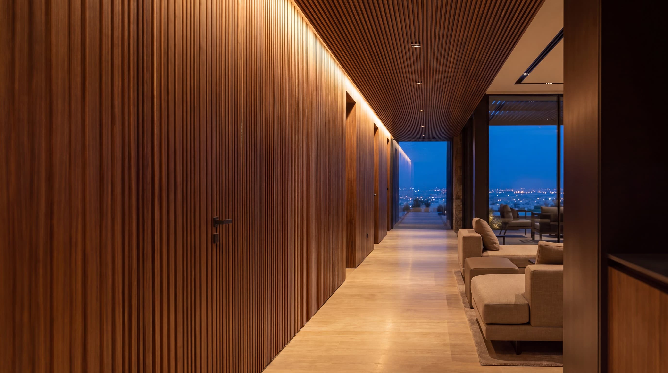 Corridor lined with fluted walnut panelling and a walnut slatted ceiling, city lights at dusk beyond